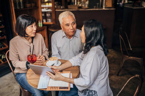 Three people, senior Taiwanese friends sitting in cafe together, using digital tablet.